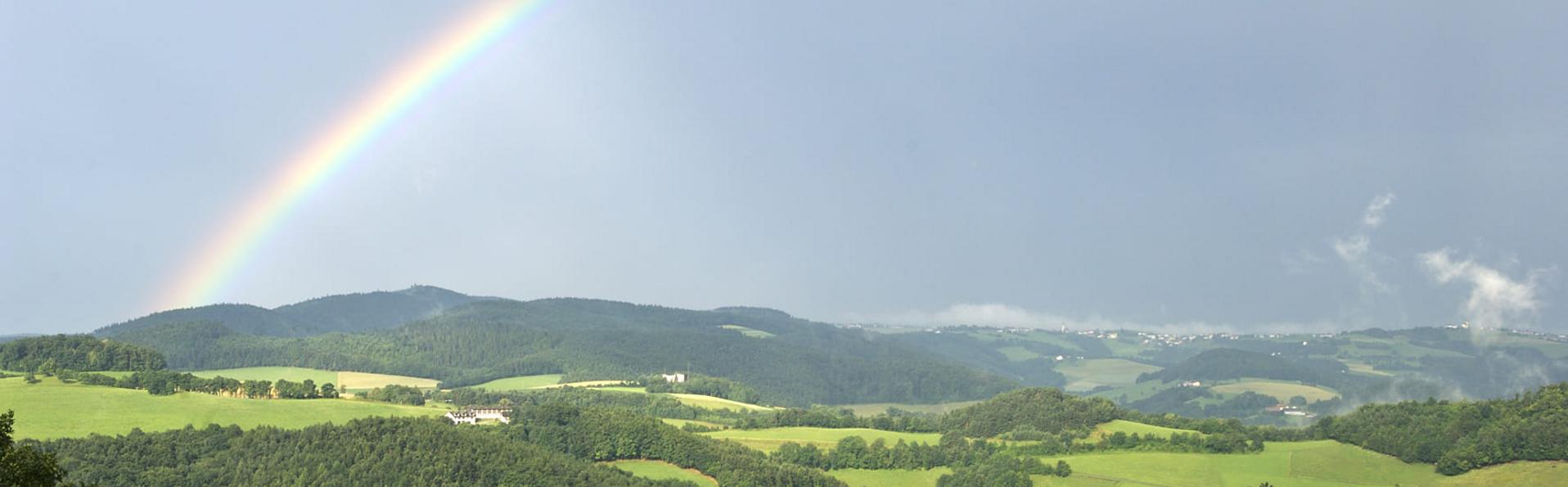 Regenbogen über sanften Hügeln mit Wäldern und Feldern